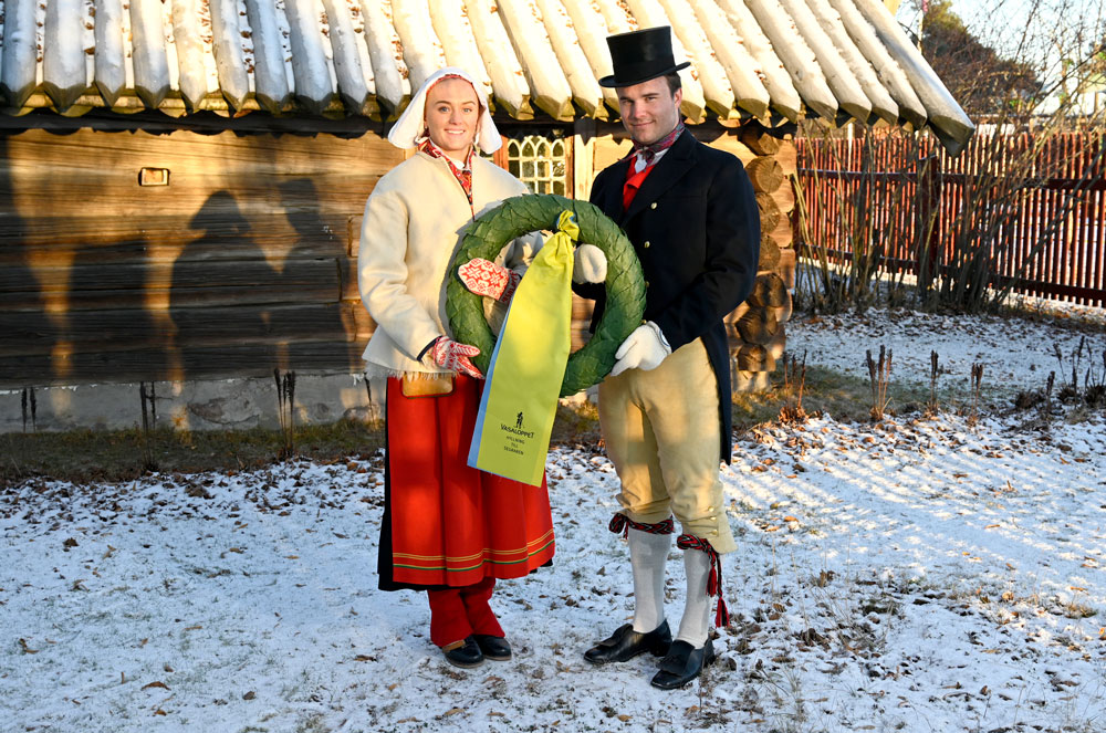 En kvinna och en man klädda i folkfräkt håller i en segrarkrans. 