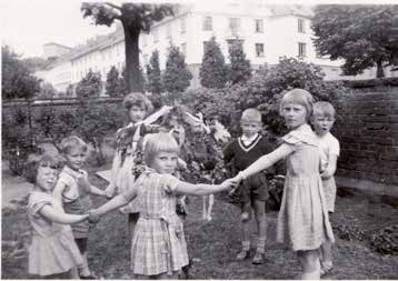 Barn håller hand i ring runt midsommarstång.
